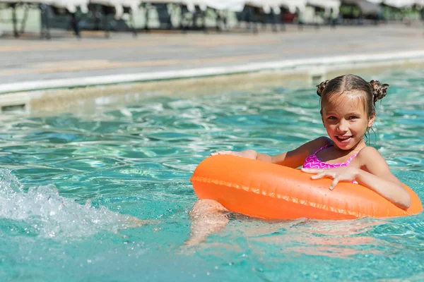 Niño nadando en la piscina en el anillo inflable y mirando la cámara - foto de stock