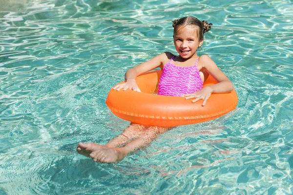 Mädchen blickt in Kamera, während sie auf aufblasbarem Ring im Schwimmbad schwimmt — Stockfoto