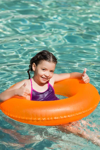 Joyful kid showing thumbs up while swimming in pool on inflatable ring — Stock Photo