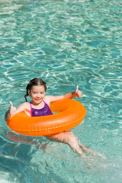 Niño alegre mostrando los pulgares hacia arriba mientras flota en la piscina en el anillo de natación - foto de stock