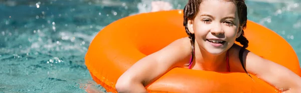 Immagine orizzontale della ragazza gioiosa che nuota sull'anello gonfiabile in piscina vicino agli spruzzi d'acqua — Foto stock