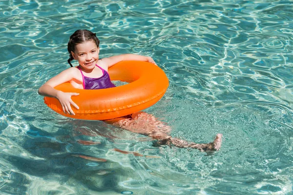Chica alegre mirando a la cámara mientras flota en la piscina en el anillo de natación - foto de stock
