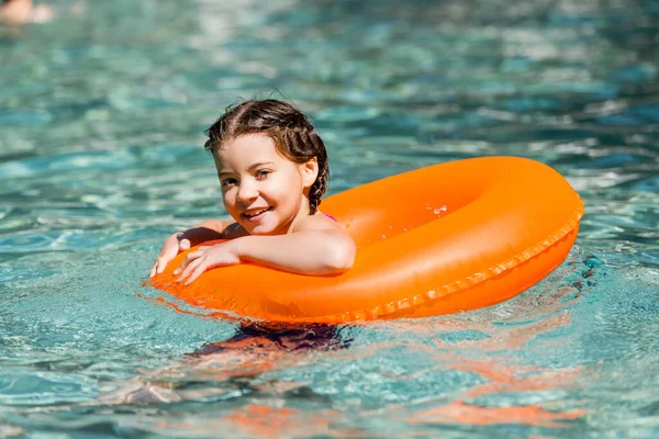 Zufriedenes Mädchen blickt in Kamera, während es im Pool auf Schwimmring schwimmt — Stockfoto