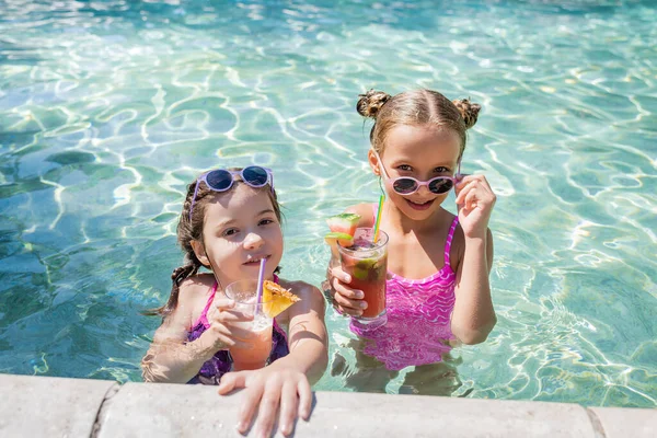 Menina tocando óculos de sol enquanto estava na piscina perto de amigo com refrescante coquetel — Fotografia de Stock