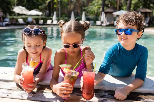 Дівчина в купальнику тримає соломинку біля друзів зі свіжими фруктовими коктейлями на березі басейну — стокове фото