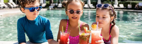 Concepto horizontal de niño y niñas en trajes de baño tintineo vasos con refrescantes cócteles cerca de la piscina - foto de stock