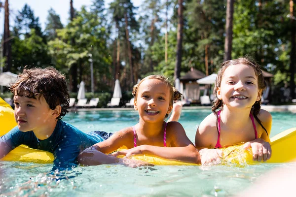 Foyer sélectif des filles joyeuses regardant la caméra tout en flottant sur matelas gonflable avec garçon — Photo de stock