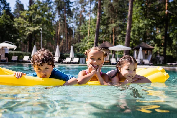 Messa a fuoco selettiva di ragazze e ragazzi che galleggiano su materasso gonfiabile in piscina — Foto stock