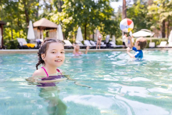 Joyeuse fille regardant la caméra tout en passant du temps dans la piscine — Photo de stock