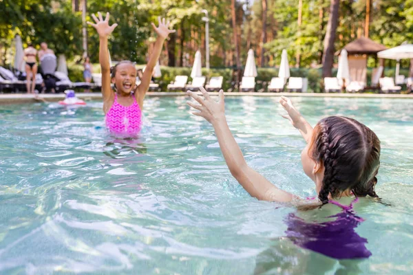 Enfoque selectivo de chica emocionada con las manos en el aire divertirse en la piscina con un amigo - foto de stock