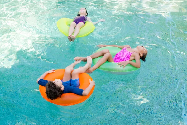 Vue grand angle des amis en maillot de bain relaxant dans la piscine sur des anneaux gonflables colorés — Photo de stock