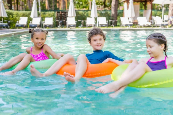 Amis joyeux nager dans la piscine sur des anneaux gonflables multicolores — Photo de stock