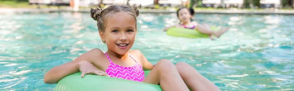 Horizontales Bild des Mädchens, das in die Kamera schaut, während es im Pool auf dem Schwimmring schwimmt — Stockfoto