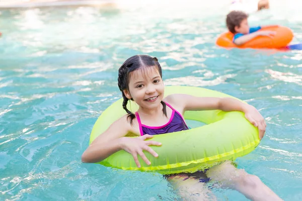 Chica alegre mirando a la cámara mientras flota en la piscina en el anillo de natación - foto de stock