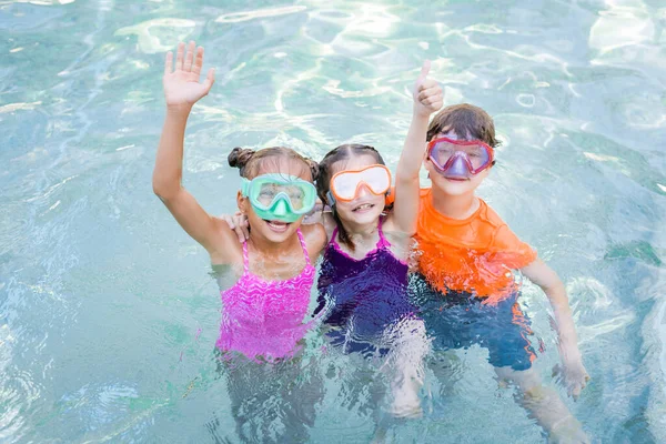 Amigos en máscaras de natación mostrando el pulgar hacia arriba y saludando la mano mientras se divierten en la piscina - foto de stock