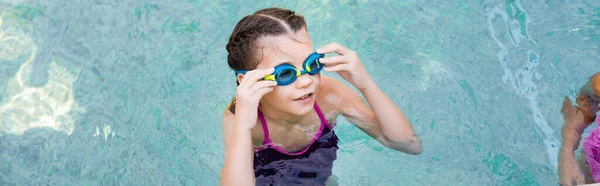 Imagen horizontal de la chica en la piscina tocando gafas de natación mientras mira hacia otro lado - foto de stock