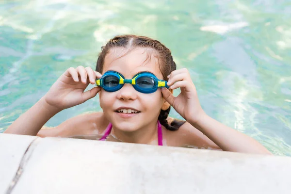 Mädchen im Pool berührt Schwimmbrille, während sie in Kamera schaut — Stockfoto