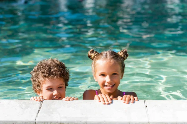 Chica mirando a la cámara mientras pasa tiempo en la piscina con chico rizado - foto de stock