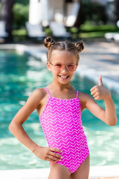 Fille en maillot de bain et lunettes de soleil tenant la main sur la hanche et montrant pouce vers le haut — Photo de stock