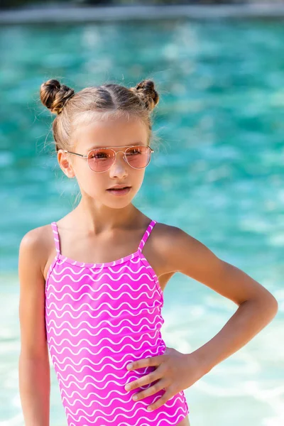 Девушка в солнечных очках и купальнике, держась за руку на бедре, отводя взгляд — стоковое фото