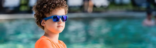 Заголовок на сайте кудрявого мальчика в синих солнцезащитных очках, отводящего взгляд — стоковое фото