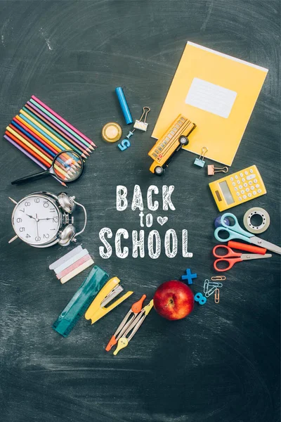 Vista dall'alto del telaio con sveglia vintage, mela verde e accessori scolastici su lavagna nera con scritte di ritorno a scuola — Foto stock