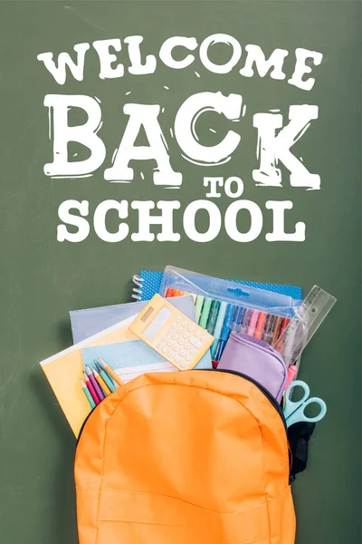 Top view of backpack packed with school stationery on green chalkboard with welcome back to school lettering — Stock Photo