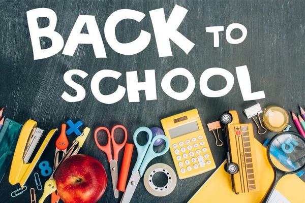 Vista dall'alto di mela matura, calcolatrice e materiale scolastico su lavagna nera con iscrizione a scuola — Foto stock