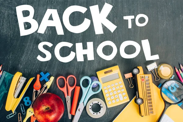 Top view of ripe apple, calculator and school supplies on black chalkboard with back to school lettering — Stock Photo