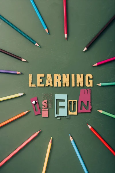 Top view of frame with color pencils on green chalkboard with learning is fun lettering — Stock Photo