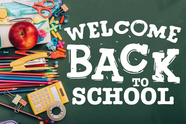 Top view of ripe apple, calculator and school stationery on green chalkboard with welcome back to school lettering — Stock Photo