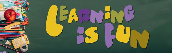 Tiro panorâmico de maçã madura, calculadora e papelaria escolar em quadro-negro verde com aprendizagem é divertido lettering — Fotografia de Stock