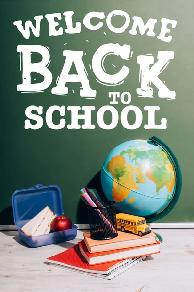 Globe near toy school bus and pen holder on books near lunch box and green chalkboard with back to school lettering — Stock Photo