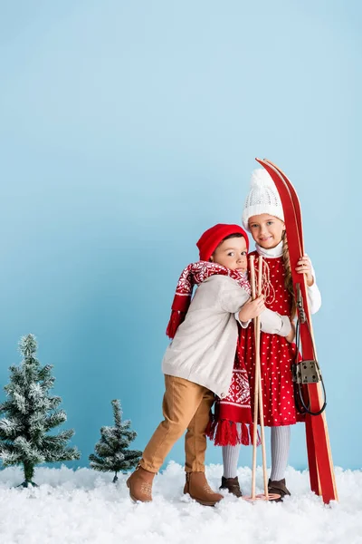 Bambino in cappello e sciarpa abbraccio sorella con bastoni da sci e sci mentre in piedi su blu — Foto stock