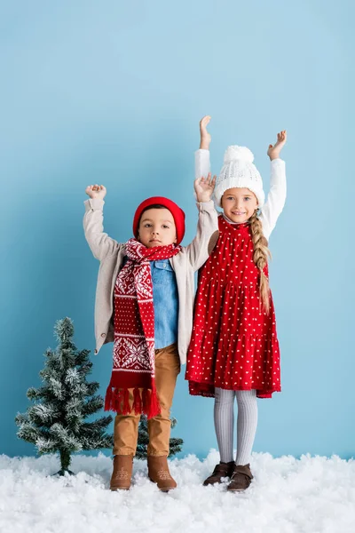 Crianças em roupa de inverno com as mãos acima das cabeças em pé no azul — Fotografia de Stock