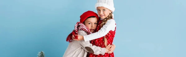 Panoramic crop of kids in winter outfit hugging near christmas tree on blue — Stock Photo