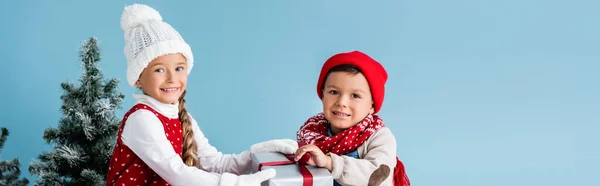 Panoramic crop of kids in winter outfit touching present isolated on blue — Stock Photo