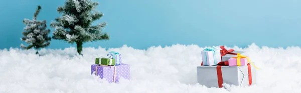 Horizontal image of presents on white snow near christmas trees isolated on blue — Stock Photo