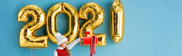 Plan panoramique de fille en chapeau prenant cadeau de boîte aux lettres près de ballons sur bleu — Photo de stock