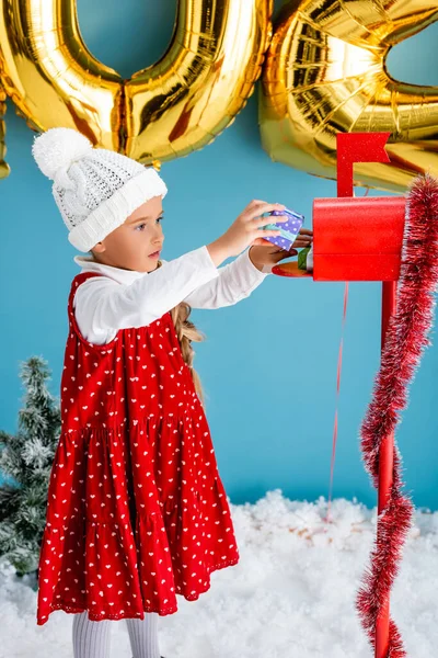 Ragazza in cappello e vestito prendendo regalo dalla cassetta postale rossa su blu — Foto stock