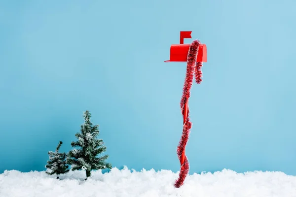 Boîte aux lettres rouge avec décoration près de pins sur neige blanche sur bleu — Photo de stock