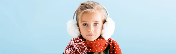 Cultivo panorámico de niño en orejeras de invierno y bufanda mirando cámara aislada en azul - foto de stock