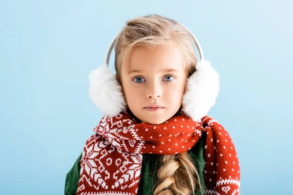 Menina no inverno earmuffs e cachecol olhando para a câmera isolada no azul — Fotografia de Stock