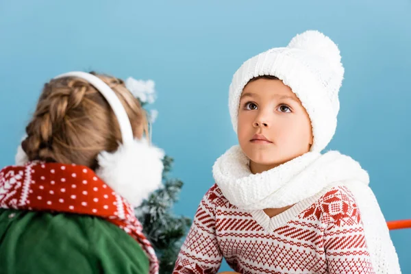 Selective focus of boy in knitted hat looking up near girl in winter earmuffs on blue — Stock Photo