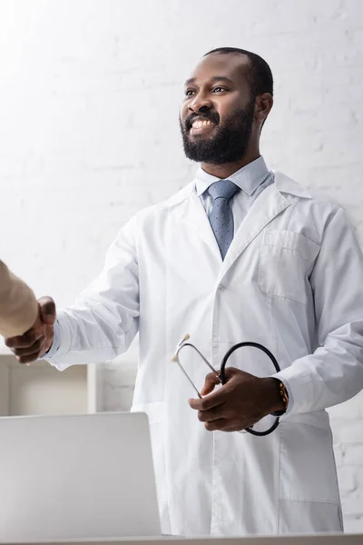 Afrikanischer Arzt hält Stethoskop in der Hand und schüttelt Patientin die Hand — Stockfoto