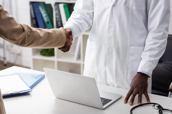 Vista recortada del médico afroamericano estrechando la mano con el paciente - foto de stock