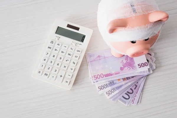 Vista superior do banco piggy com atadura no dinheiro perto da calculadora — Fotografia de Stock
