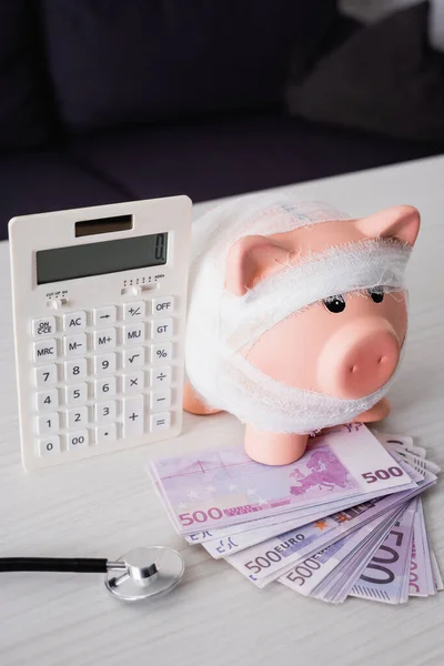 Selective focus of piggy bank with bandage on money near calculator — Stock Photo