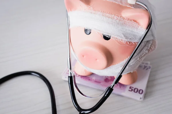 Selective focus of piggy bank on money with stethoscope on white table — Stock Photo