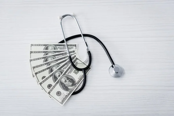 Top view of stethoscope and dollar banknotes on white table — Stock Photo